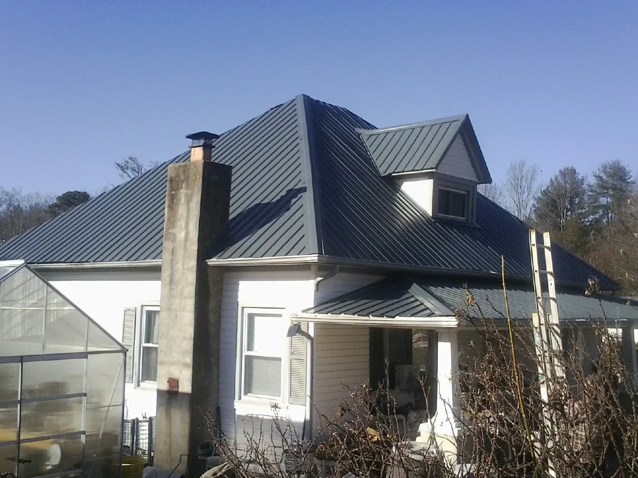 Dark blue standing seam metal roof on a white farmhouse with dormer — Slate & Tile Roof Repair by Roofing Brothers in Saint Clair