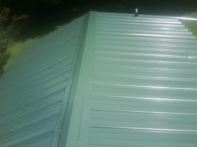 New green metal panels meeting at the ridge of a roof — Flat Roof Repair work by our crew in Saint Clair