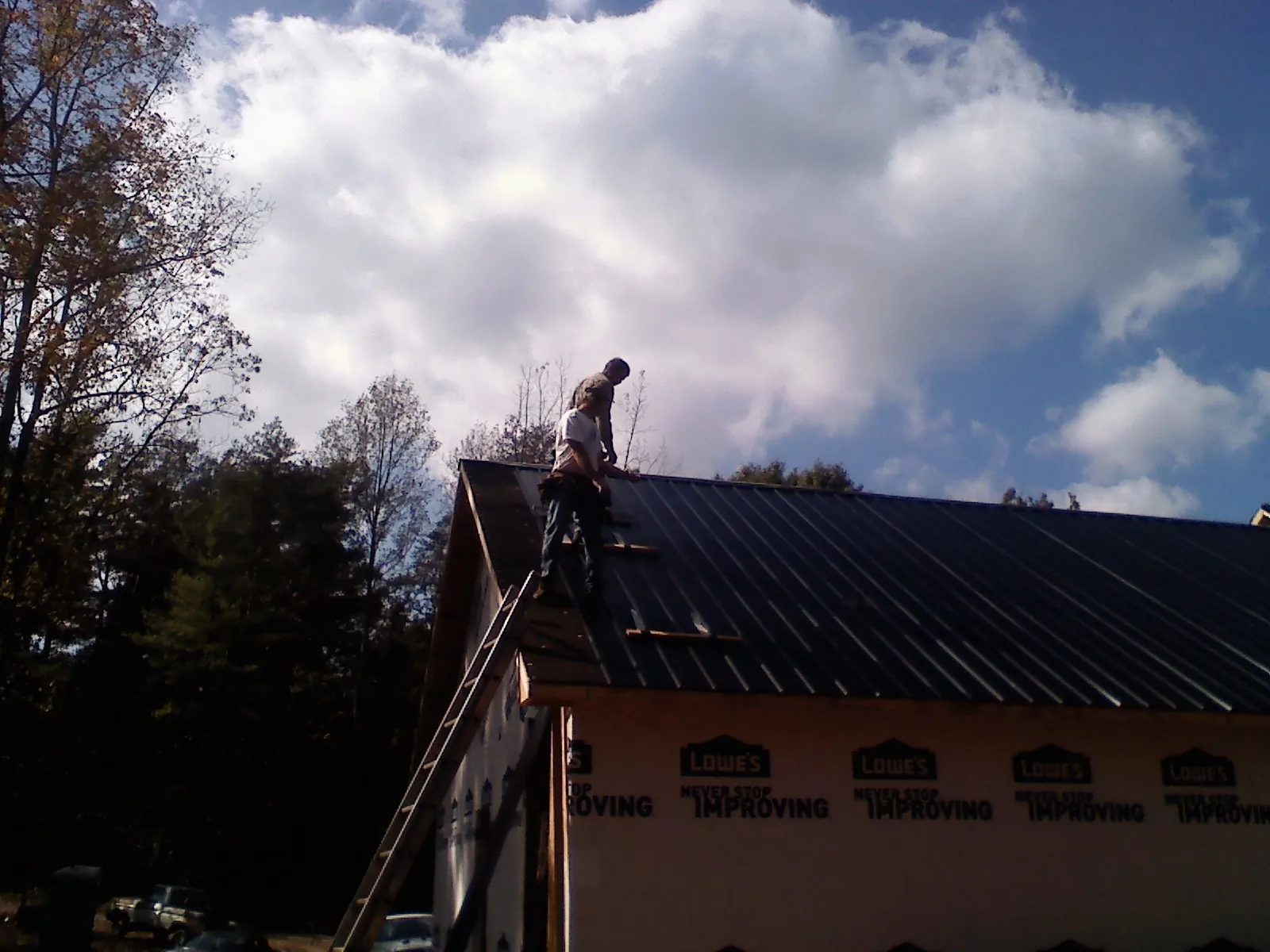 Roofer fastening dark metal panels high against a cloudy sky, from a Roof Inspection job in Saint Clair